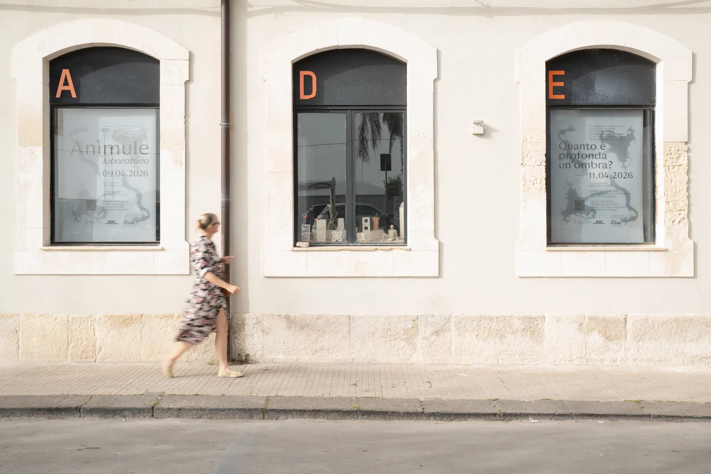 Anìmule posters in the windows of MADE Program, a woman walking past